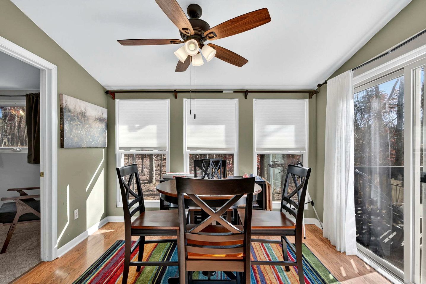 A dining area with a ceiling fan, a table with chairs, and large windows with blinds.