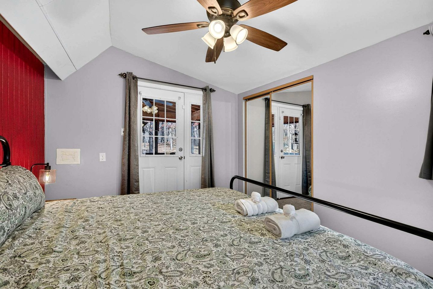 Une chambre à coucher avec une couvre-lit à motifs, un ventilateur de plafond, un miroir et une porte donnant sur une vue agréable.