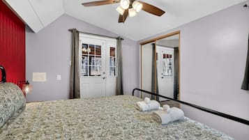 Une chambre à coucher avec une couvre-lit à motifs, un ventilateur de plafond, un miroir et une porte donnant sur une vue agréable.