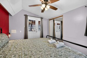 Une chambre à coucher avec une couvre-lit à motifs, un ventilateur de plafond, un miroir et une porte donnant sur une vue agréable.