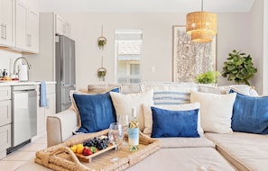 A modern living room with a sofa set, a dining table with a fruit and cheese board, and a wine bottle. - Coastal Cool - Relaxing Crystal Beach Getaway with Balcony & Pool (Destin)