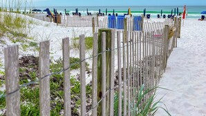 Ein sandiger Strand mit einer Holzlattenzaun und Liegestühlen.