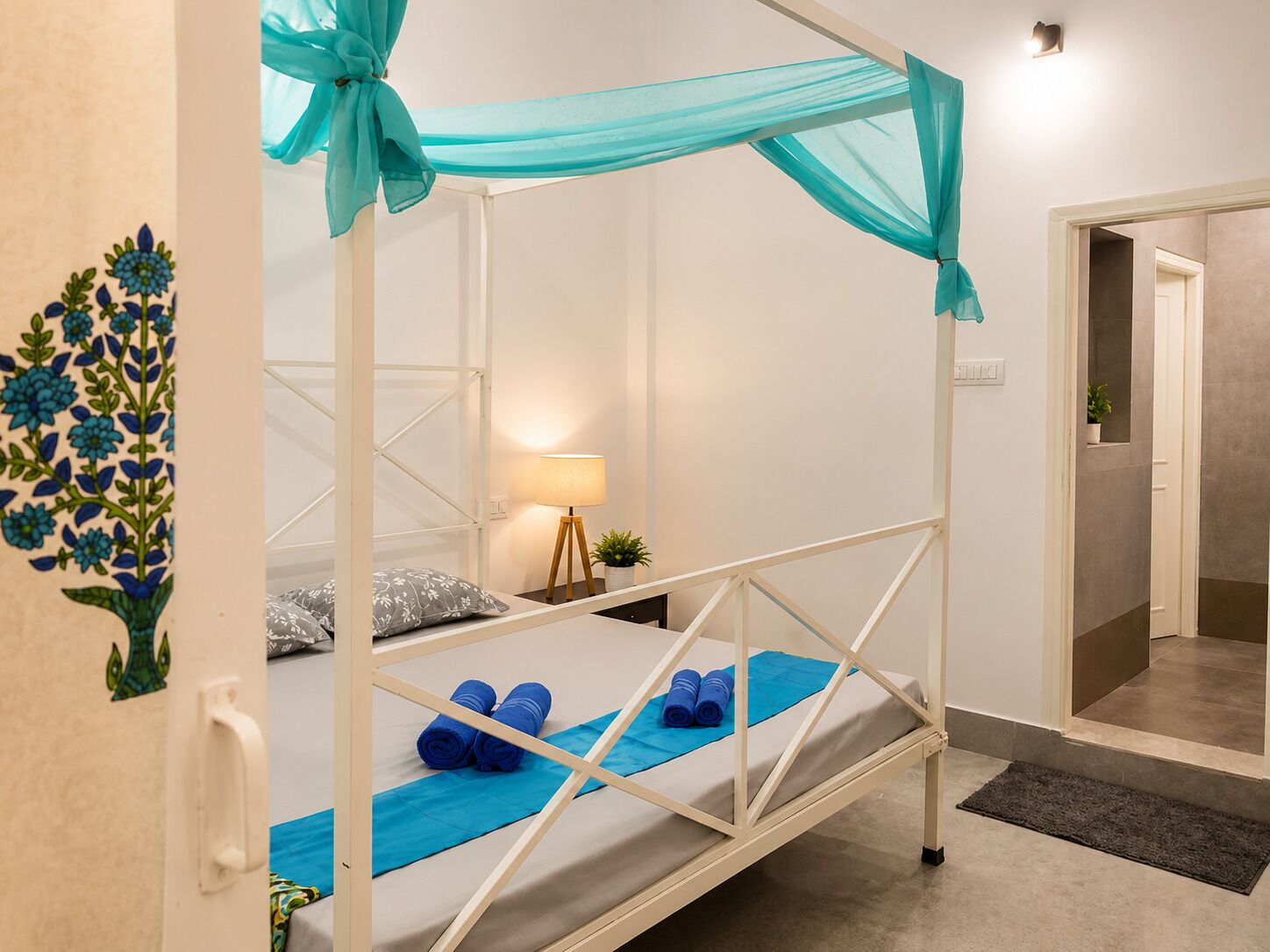 Ein Einzelzimmer mit Baldachinbett, Nachttischlampe, kleiner Topfpflanze und einer Wanddekoration.