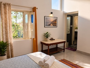 A hotel room with a bed, a table with a plant, a window with curtains, and a painting on the wall. - Hotel Atithya (Udaipur)