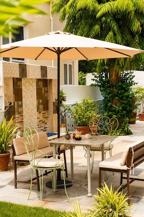 An outdoor patio with a table and chairs, a large umbrella, and potted plants. - Hotel Atithya (Udaipur)