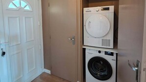 A laundry room with a front-loading washer and dryer, a white door with a glass panel, and a hanging light fixture.