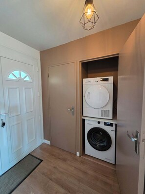 A laundry room with a front-loading washer and dryer, a white door with a glass panel, and a hanging light fixture.