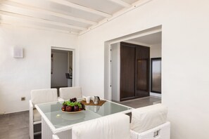 A modern dining area with a glass-top table, white wicker chairs, and a bowl of fruit. - Casa Foti Puerto del Carmen - Media estancia (Puerto del Carmen)