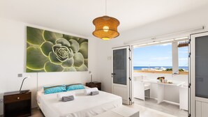 Et soveværelse med en stor seng, et natbord, et vindue med udsigt til stranden.