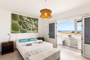 A bedroom with a large bed, a bedside table, a nightstand, a large window, and a view of the beach. - Casa Foti Puerto del Carmen - Media estancia (Puerto del Carmen)