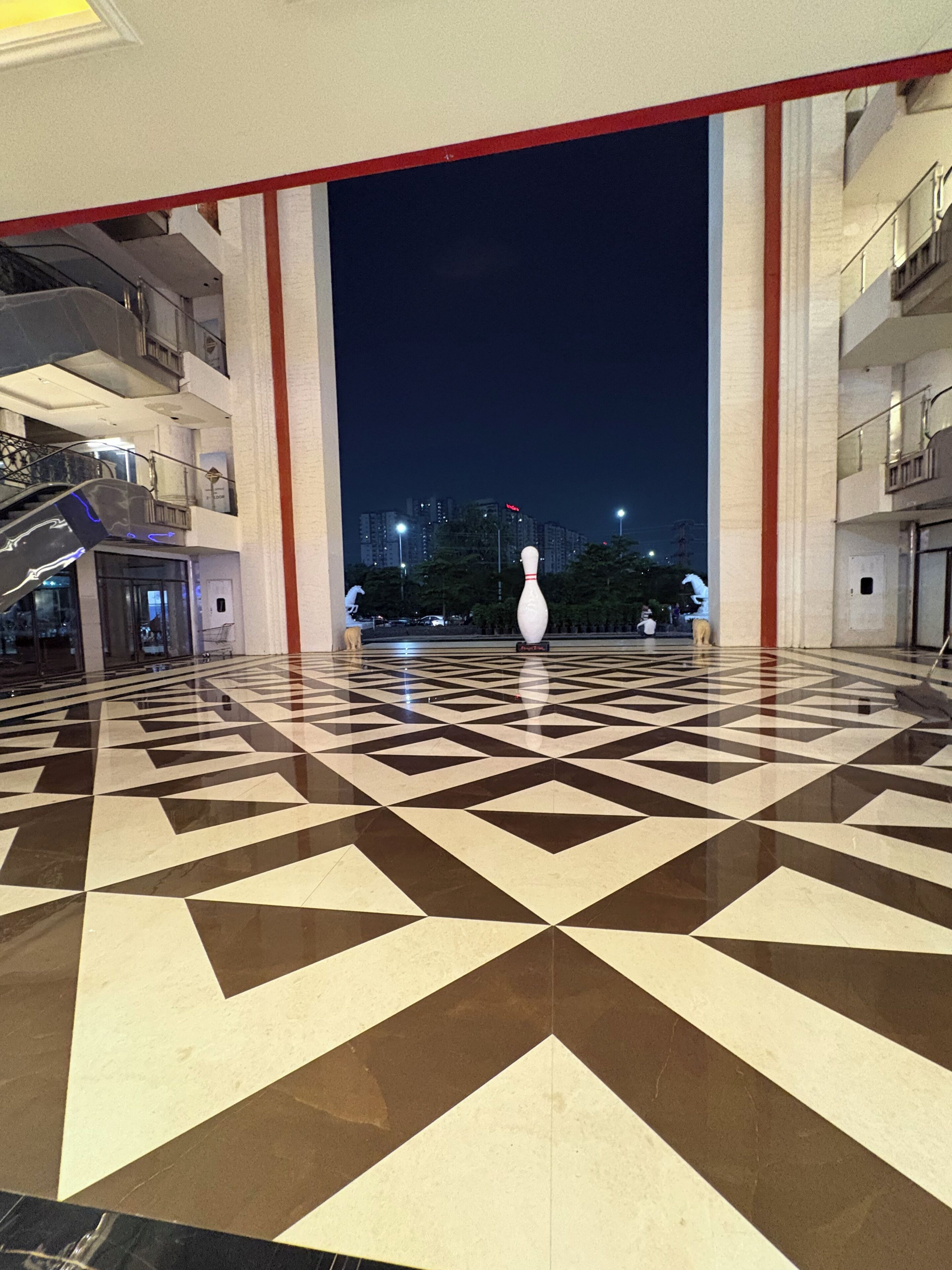 Un hall d’entrée spacieux, doté d’un sol aux motifs géométriques, d’une sculpture blanche au centre et offrant une vue sur le paysage urbain illuminé la nuit.