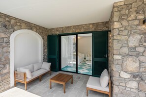 A room with stone walls, a wooden bench, two sofas, and a view through a glass door. - Estate4home - Villa Nerea (Massa Lubrense)