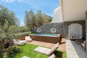 Ein Pool mit Steinmauer, Sitzgelegenheiten im Freien und Blick auf Bäume und Berge.