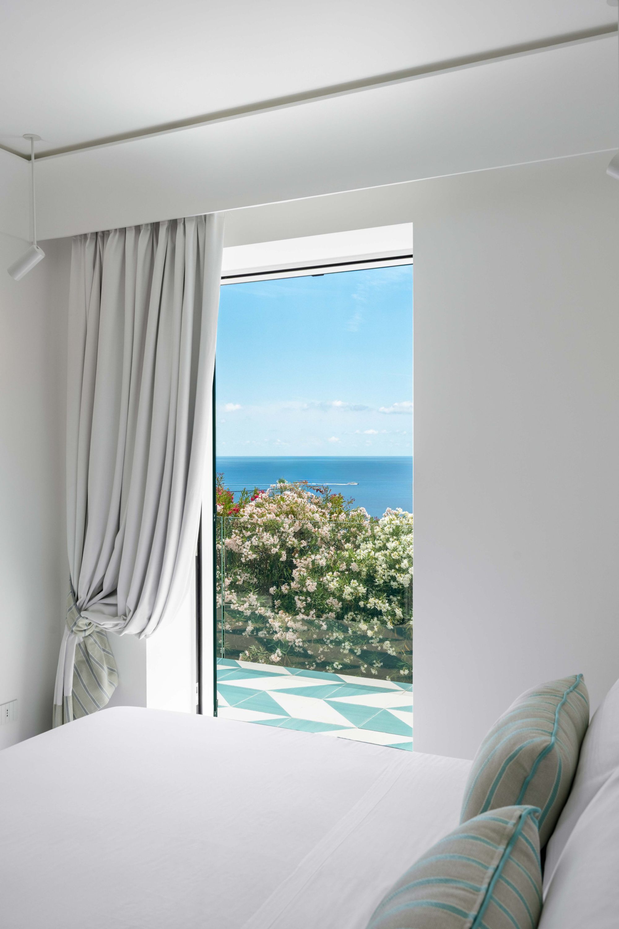 A bedroom with a large bed, a window with curtains, and a view of the sea.