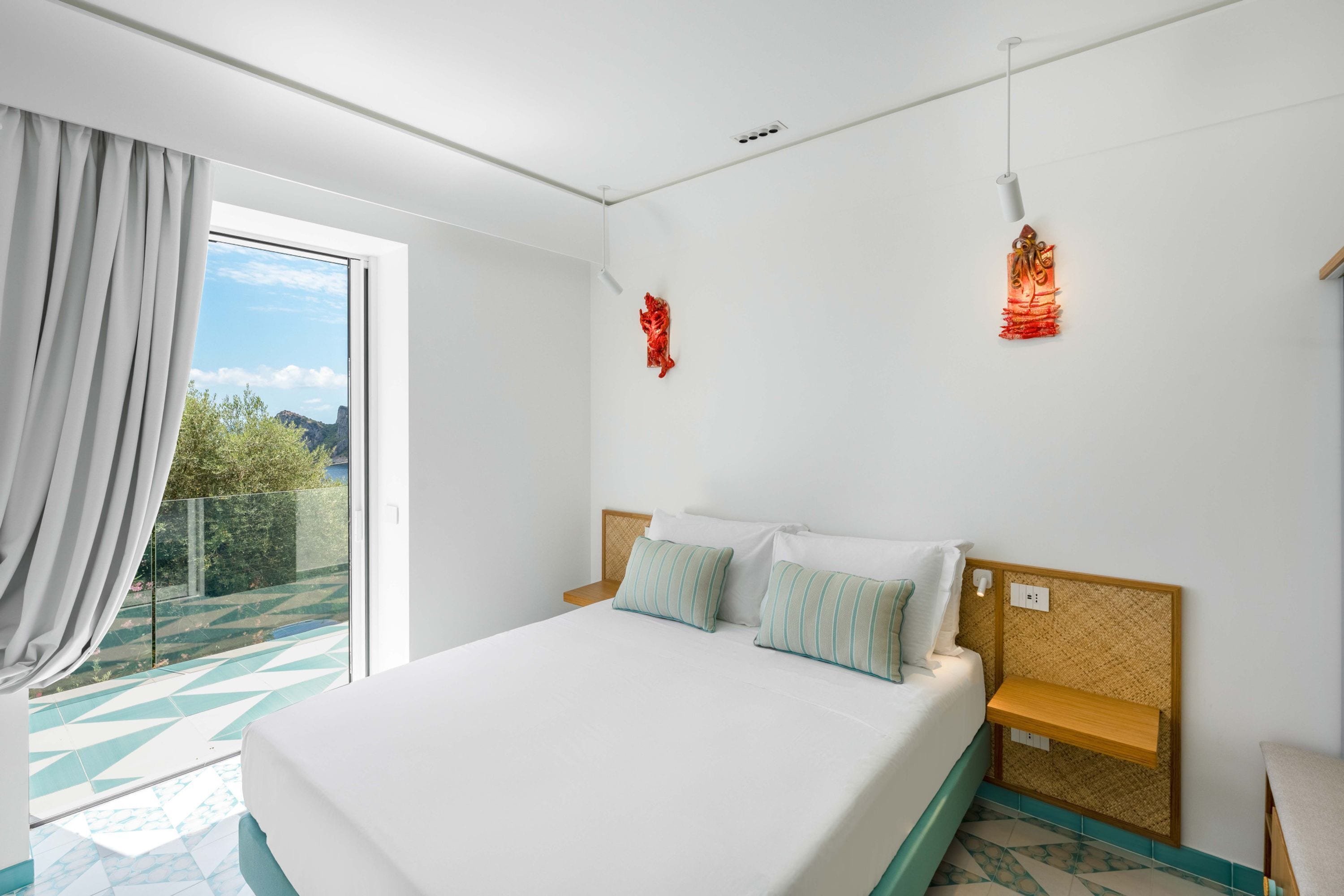 Habitación de hotel con cama, mesita de noche, lámpara de pared y vistas al exterior.