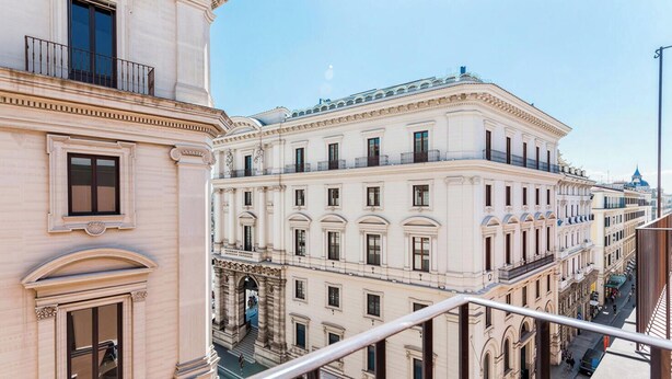Ein mehrstöckiges Gebäude mit klassischer Architektur, das Balkone und einen zentralen Eingang mit Säulen aufweist.
