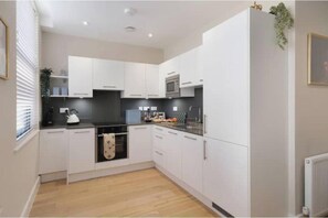 A modern kitchen with white cabinets, a black countertop, and a built-in oven. - Stylish City Living in the Heart of Historic Bath | Modern One-Bed Apartment (Bath)