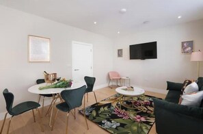 Ein modernes Wohnzimmer mit Essbereich, einem an der Wand befestigten Flachbildfernseher und einem floralen Teppich.