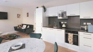 Una cucina moderna con mobili bianchi, un forno a microonde e una lavastoviglie. C'è un'area pranzo con un tavolo rotondo e sedie.