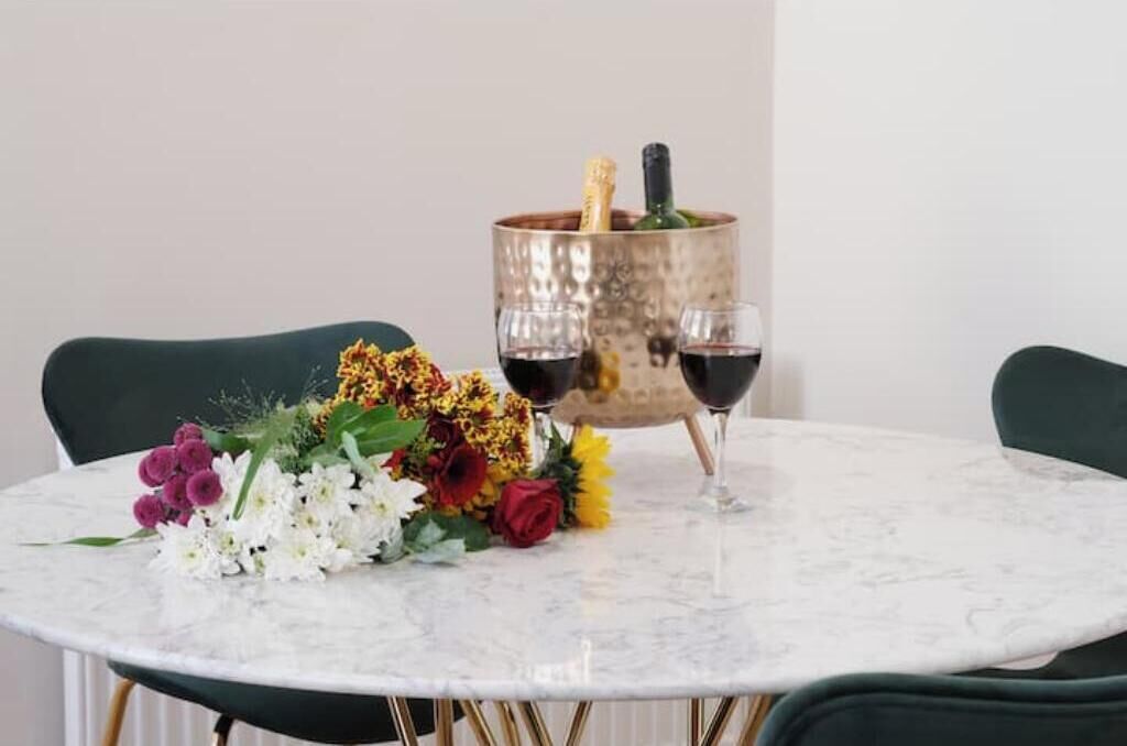 Ein runder Tisch mit Marmorplatte, zwei Stühle, eine Blumenkomposition, eine Champagnerflasche und zwei Weingläser.