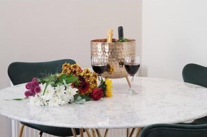 Ein runder Tisch mit Marmorplatte, zwei Stühle, eine Blumenkomposition, eine Champagnerflasche und zwei Weingläser.