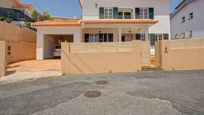 A two-story house with a covered garage, a gated entrance, and a clear sky. - Holiday Home 'Villa da Pena' with Jacuzzi and Air Conditioning (Funchal)