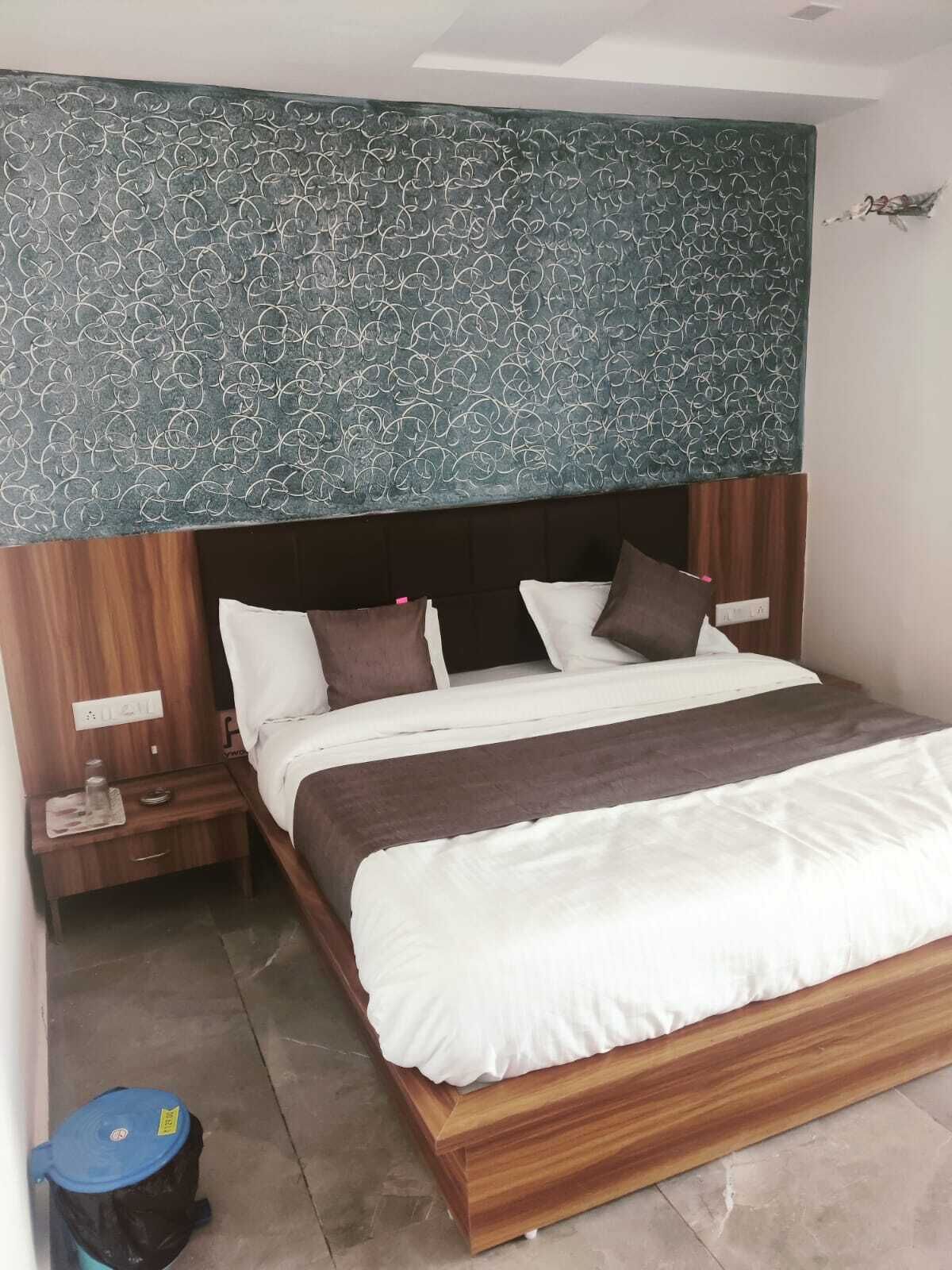 A hotel room with a large bed, wooden headboard, and a patterned wall above the bed.