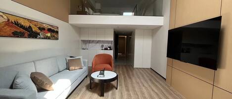 Un intérieur moderne avec un canapé, un fauteuil, une petite table et un téléviseur fixé au mur.
