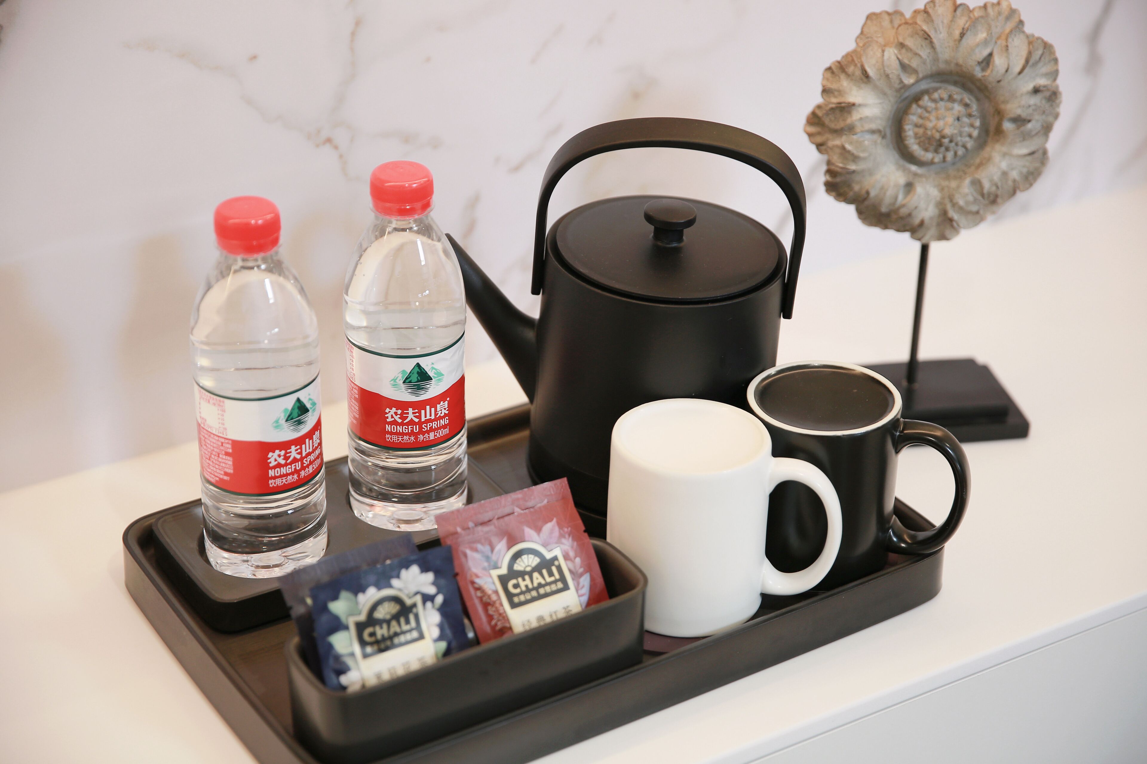 Una bandeja con dos botellas de agua, una tetera negra, una taza blanca y bolsitas de té.