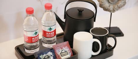A tray with two water bottles, a black kettle, a white mug, and some tea bags.