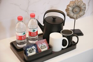 A tray with two water bottles, a black kettle, a white mug, and some tea bags. - Poltton International Apartment Hotel (Wuhan High-Speed Rail Station West Square Happy Valley) (Wuhan)