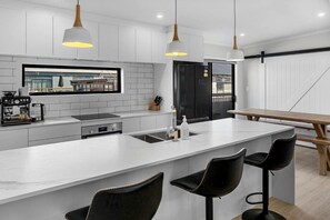 A modern kitchen with a large island, bar stools, pendant lighting, and a view of the city through a window. - Luxury Glamping near Wahihi Beach for Amazing Family Vacations in New Zealand (Waihi Beach)