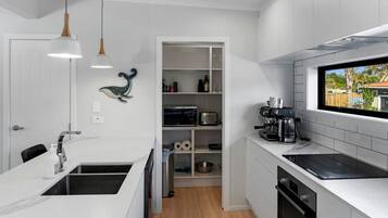 Une cuisine moderne avec des meubles blancs, un four encastré, une machine à café et une fenêtre offrant une belle vue.