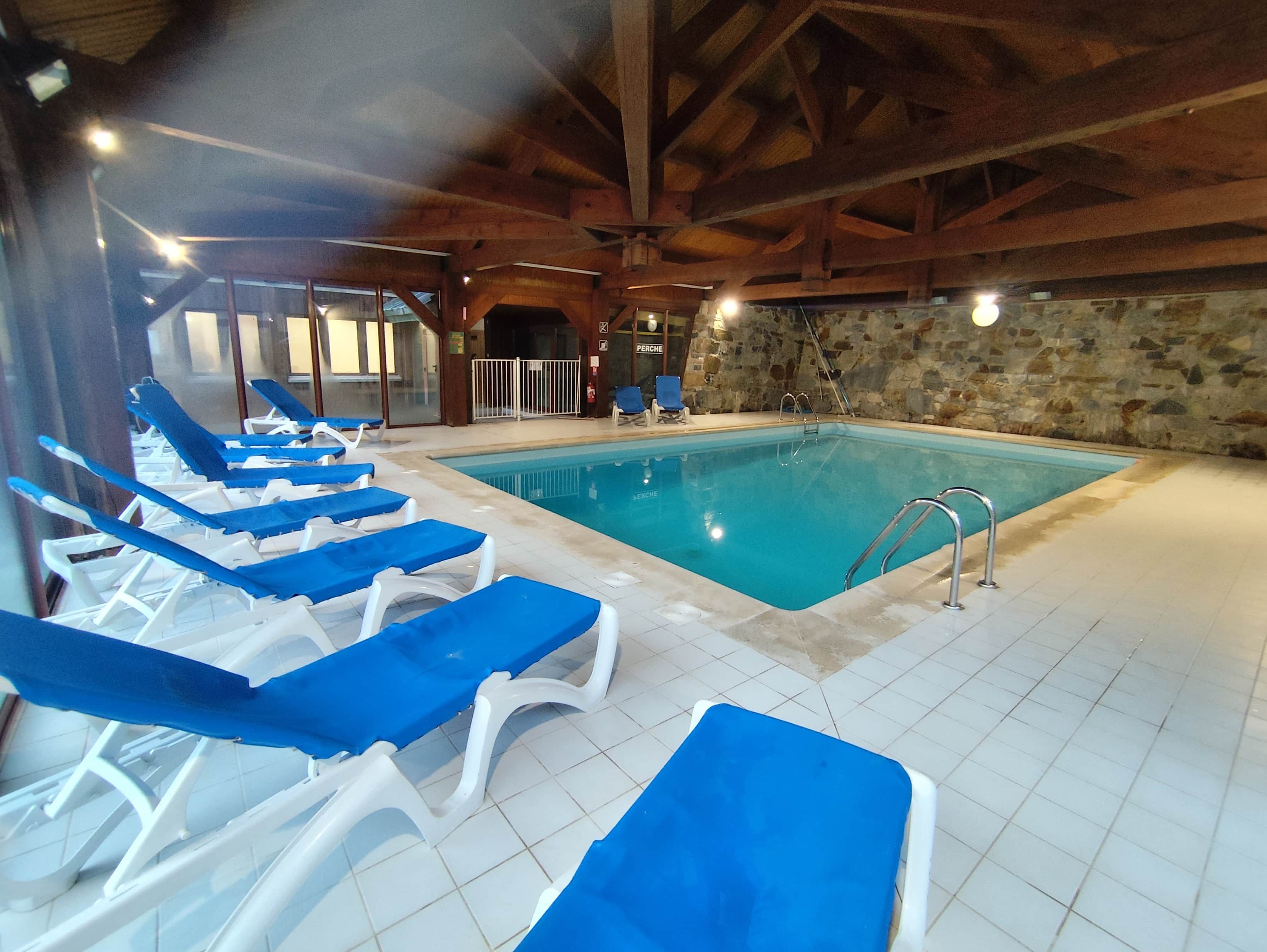 Una piscina interior con sillas de descanso azules y paredes de piedra.