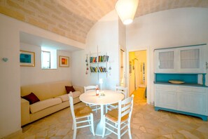 Ein gemütliches Zimmer mit einem weißen runden Tisch, weißen Stühlen, einem beigefarbenen Sofa, einem Bücherregal und einem blauen Schrank.