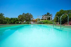 Ein klares, blaues Schwimmbecken mit einem weißen Gebäude im Hintergrund, umgeben von viel Grün.