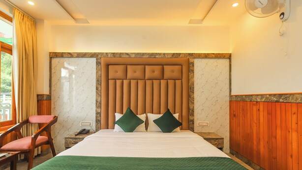 A hotel room with a large bed, a wooden headboard, a green bedspread, a wooden nightstand, a telephone, and a chair. - BR Resort (Dharamshala)