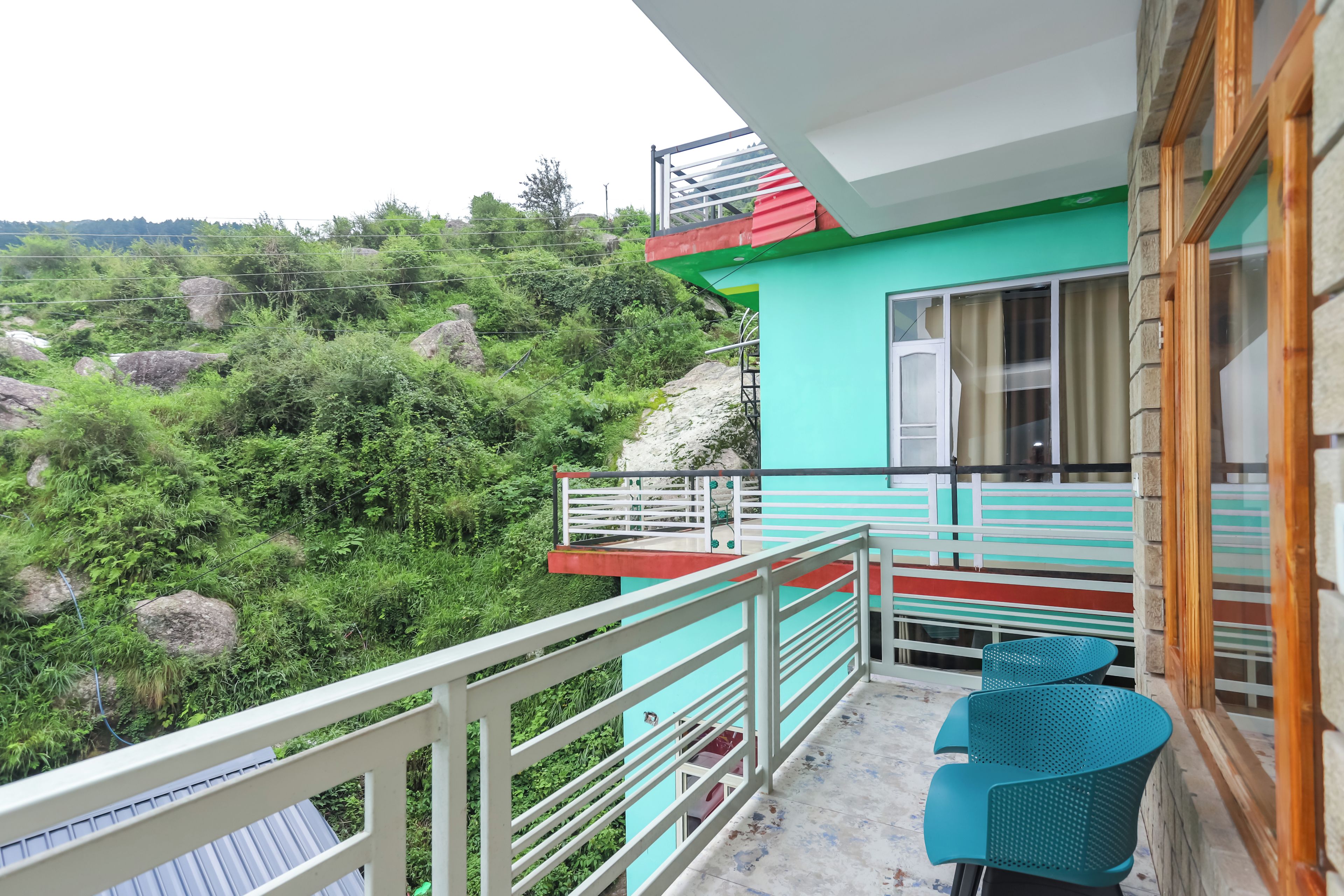 A balcony with a view of a mountainous landscape, a small seating area with chairs, and a door leading to the interior.