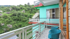 A balcony with a view of a mountainous landscape, a small seating area with chairs, and a door leading to the interior. - BR Resort (Dharamshala)