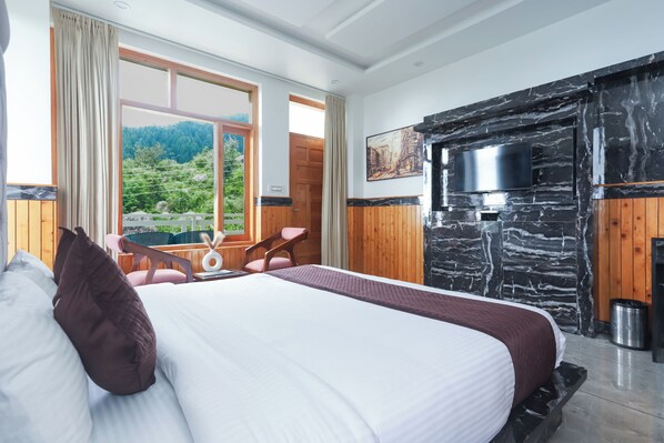 Un dormitorio con una cama, un televisor instalado en una pared de piedra, una ventana con vistas a la vegetación y una puerta de madera.