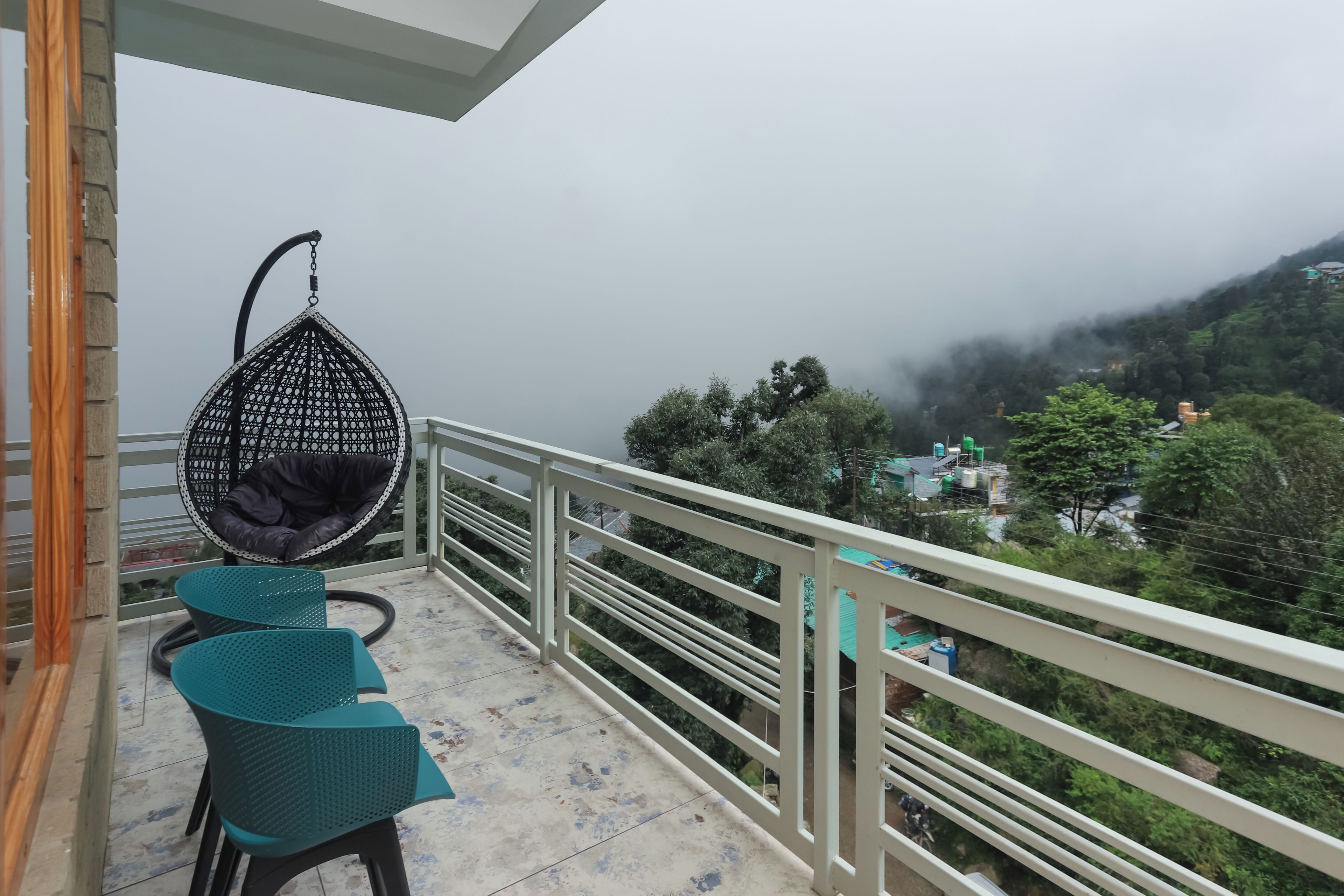 Un balcon avec un fauteuil suspendu, deux chaises et une vue sur un paysage montagneux.