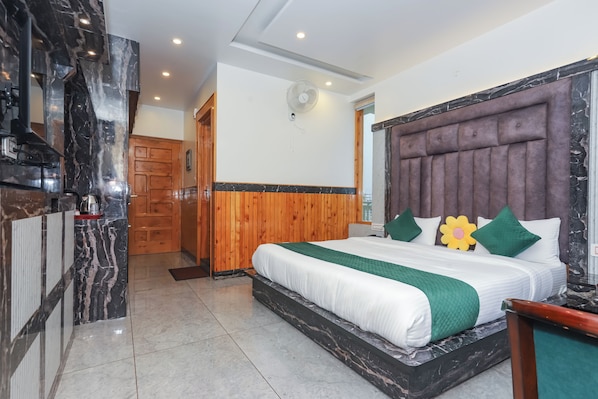 A hotel room with a marble accent wall, a wooden door, a bed with a green quilt, and a marble headboard.