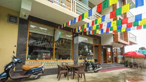 A restaurant with outdoor seating, a motorcycle parked in front, and colorful prayer flags hanging above. - BR Resort (Dharamshala)
