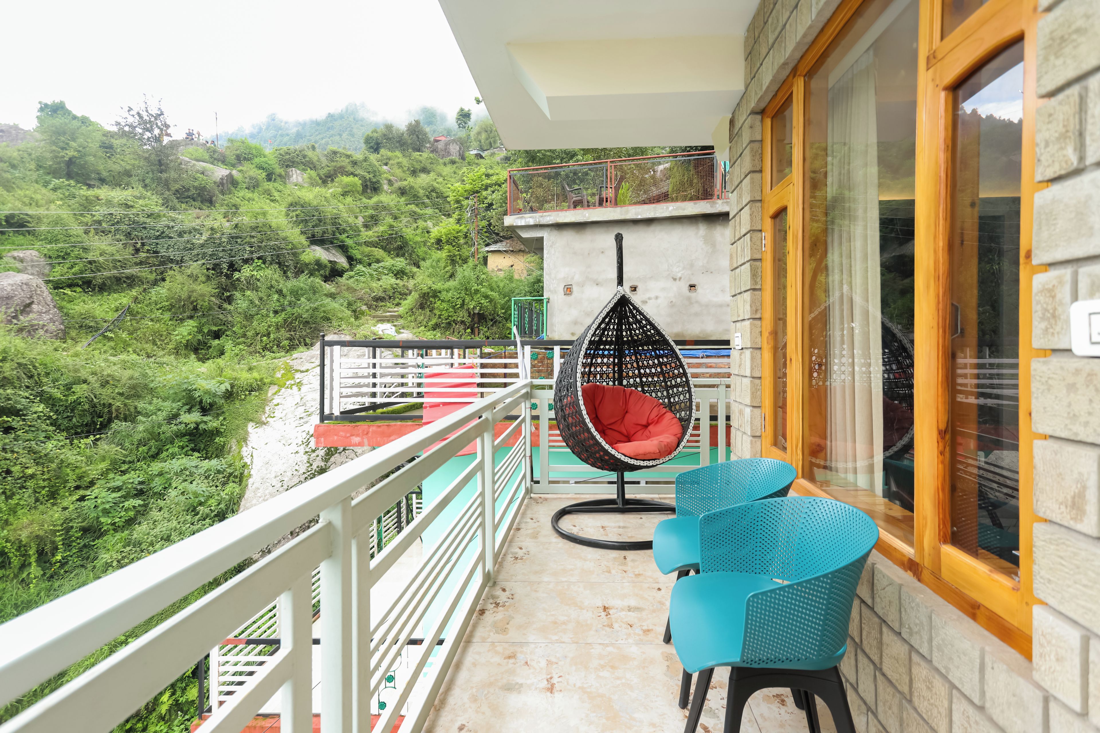 A balcony with a hanging chair, two chairs, and a view of a lush green landscape.