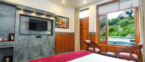 A hotel room with a bed, a TV mounted on the wall, a painting, a wooden door, and a view of greenery outside.