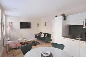 A modern living space with a dining area, a sofa, a TV, and a kitchen area. - Modern Two-Bed Apartment in Central Bath (Bath)