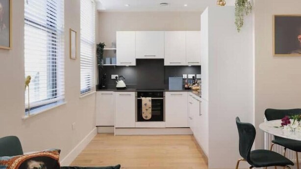 A modern kitchen with white cabinets, a black countertop, and a dining area with a round table and chairs. - Modern Two-Bed Apartment in Central Bath (Bath)