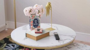 A round table with a vase of flowers, a book, a remote control, and a decorative bird on a stand. - Modern Two-Bed Apartment in Central Bath (Bath)
