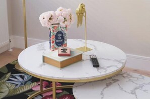A round table with a vase of flowers, a book, a remote control, and a decorative bird on a stand. - Modern Two-Bed Apartment in Central Bath (Bath)