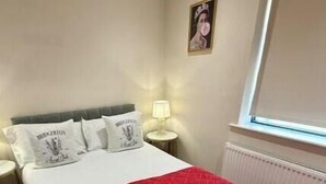 A bedroom with a bed, a red blanket, a nightstand with a lamp, and a window with blinds. - Modern Two-Bed Apartment in Central Bath (Bath)
